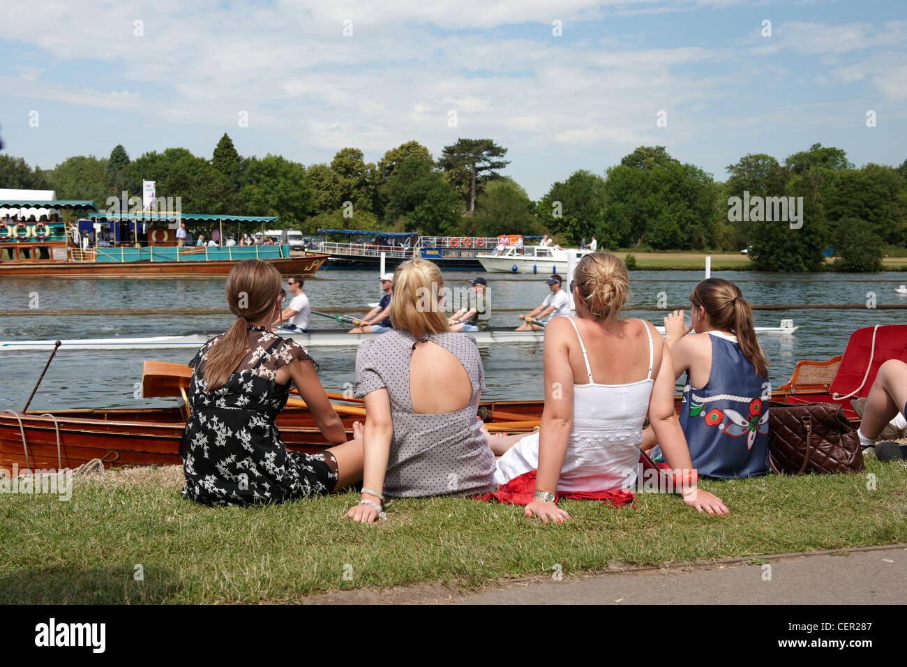 Vier junge Frauen sitzen am Ufer des Flusses genießen die jährliche Henley Royal Regatta. Stockfoto