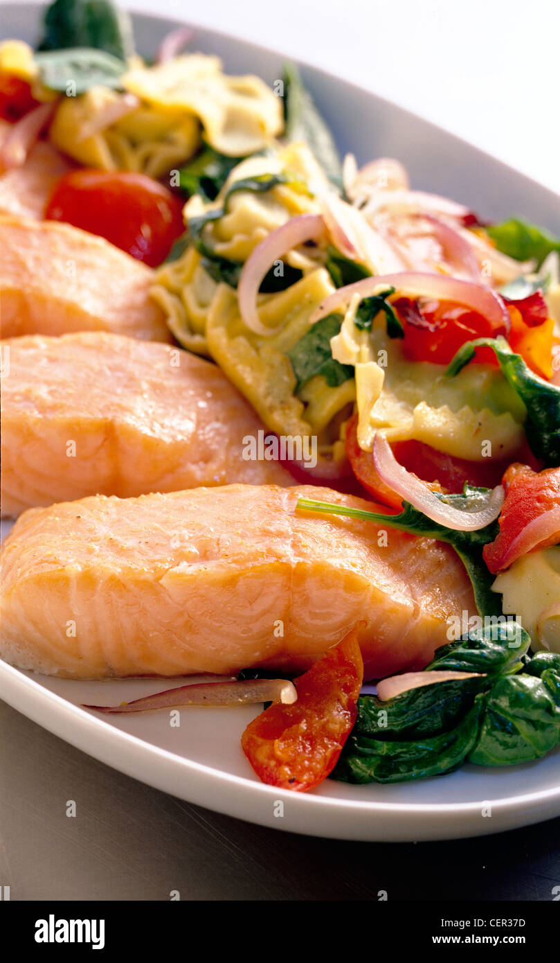 Unter der Woche Mahlzeiten gebackene Lachs warm Tortellini Salat, roten Zwiebeln, frischem Spinat und Tomaten, in großen weißen Teller gegen weiß Stockfoto
