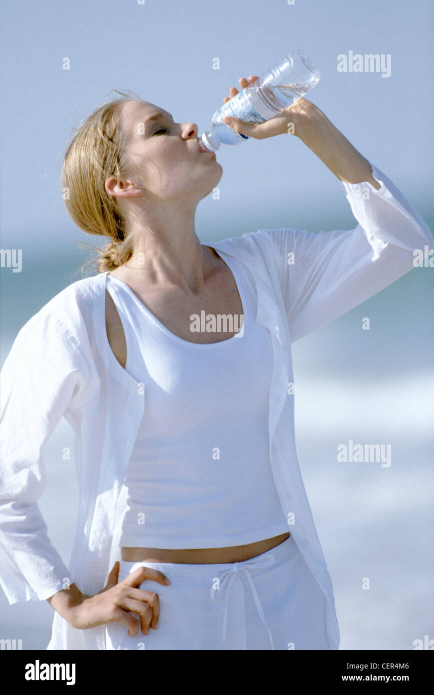 Weibliche blonde Haare aus Gesicht tragen weiße Weste Top, weiße Bluse und weiße  Baumwollhose, trinken aus der Flasche Wasser Stockfotografie - Alamy
