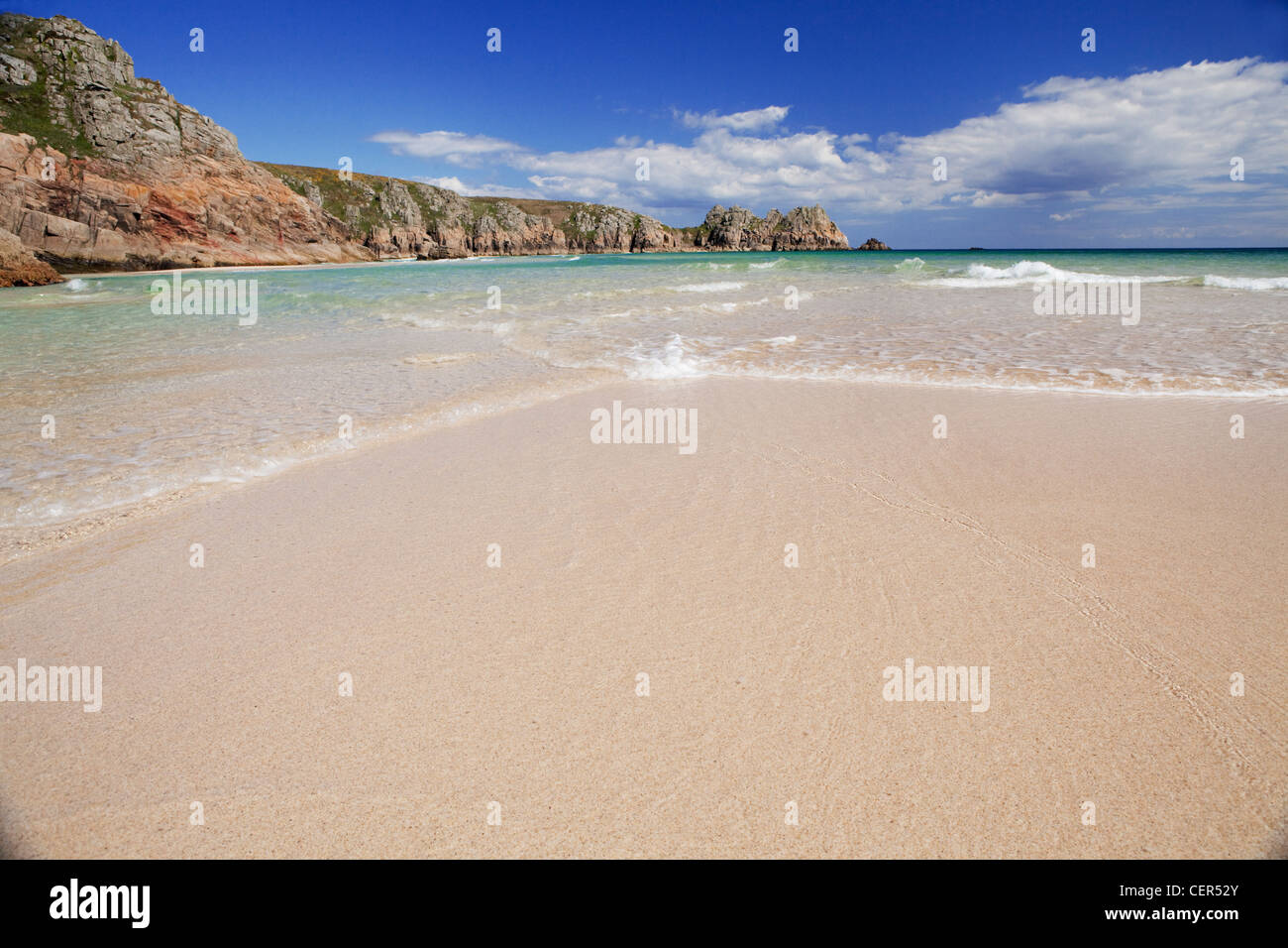 Ebbe am sandigen Strand von Porthcurno mit Logan Rock in der Ferne. Stockfoto