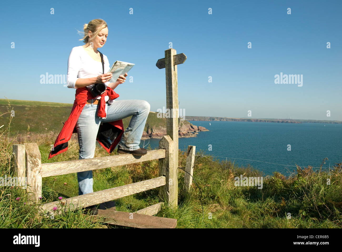 Eine weibliche Walker hält an einen Stil mit Karte über St. Annen Kopf an der Küste von Pembrokeshire. Stockfoto