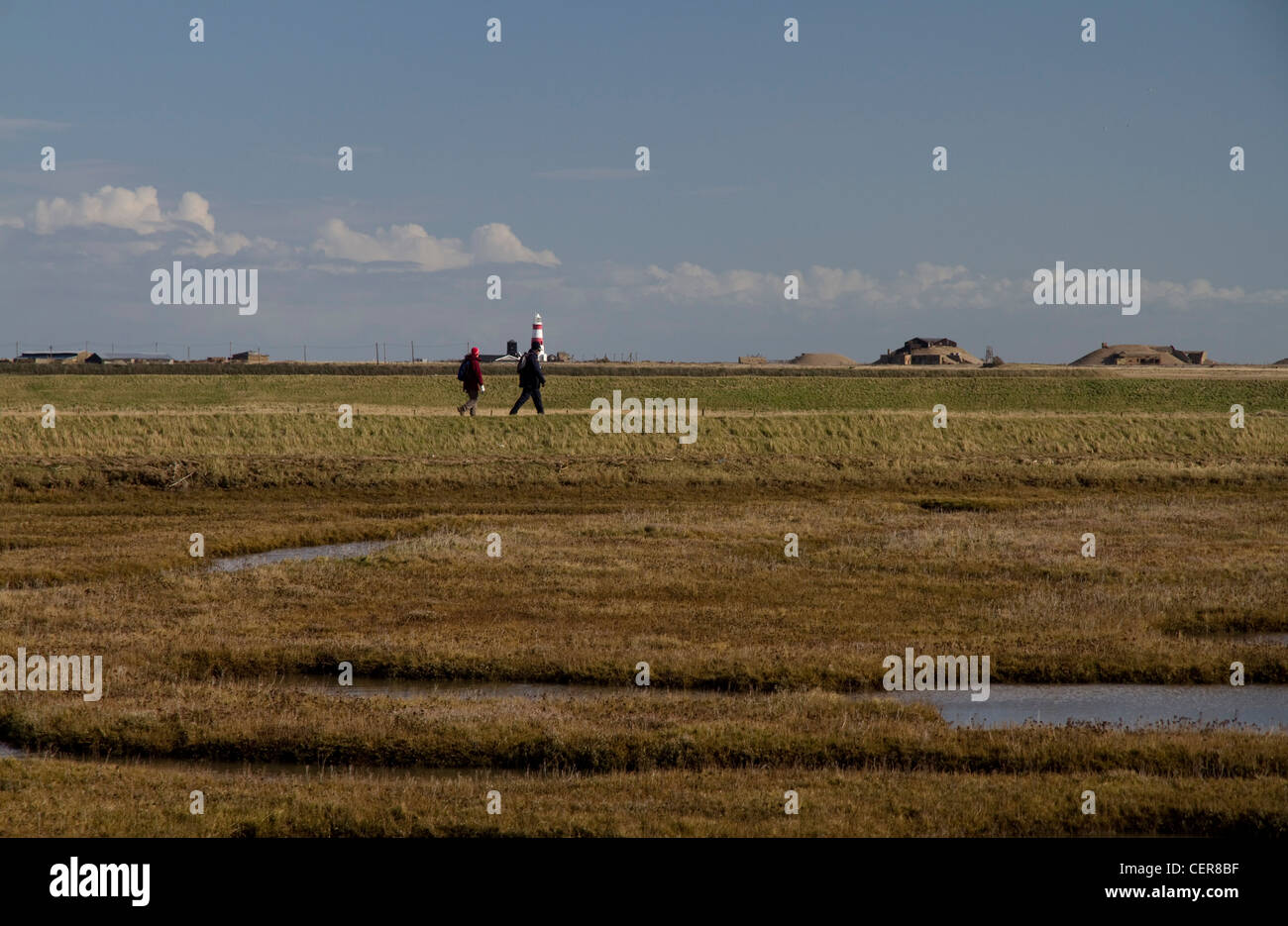 Wanderer auf dem Deich in Orford mit Orford Ness und dem Leuchtturm im Hintergrund, Suffolk, England Stockfoto