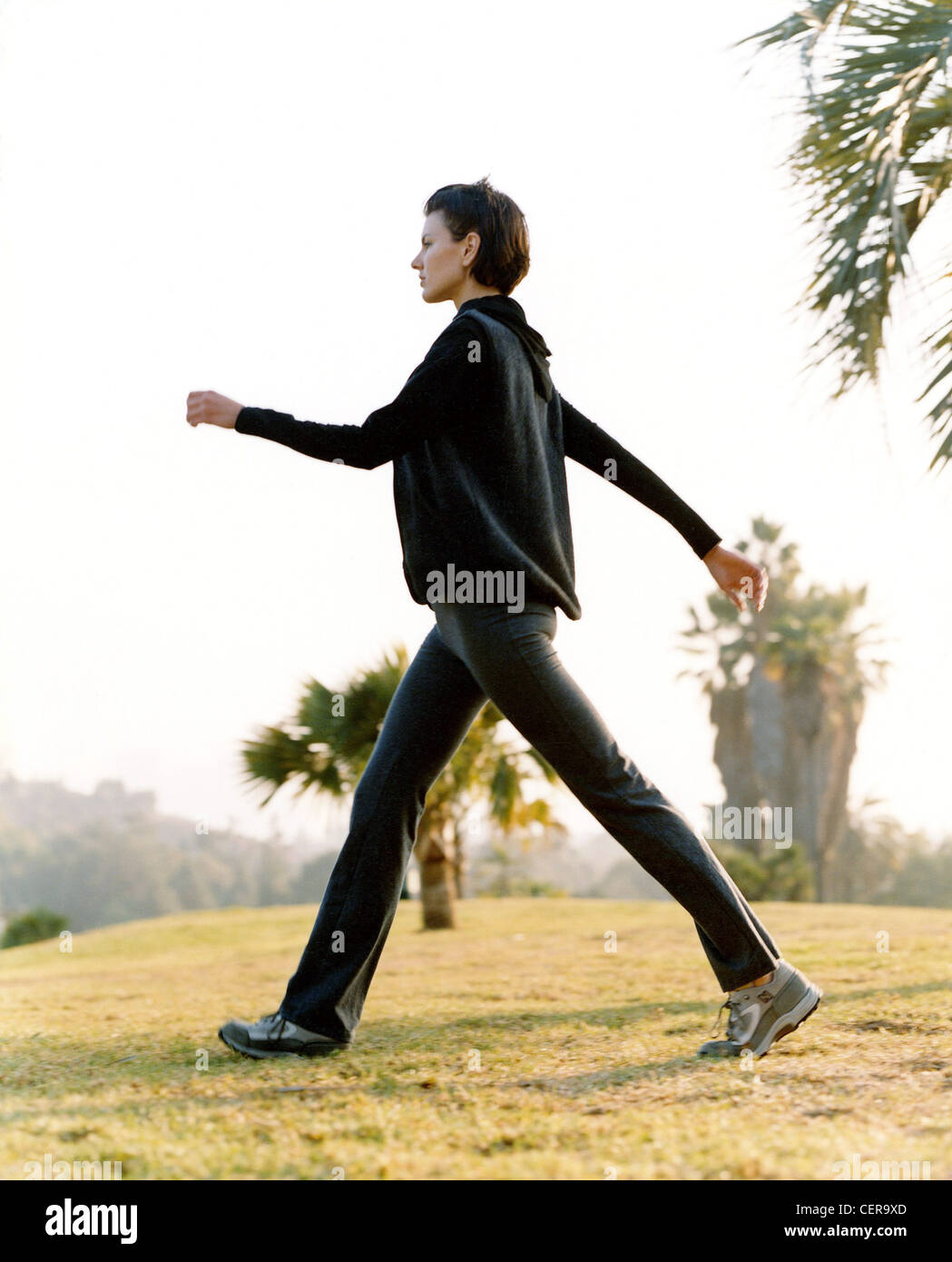 Frauen kurze Haare Powerwalking in einem Feld schwingen beide Arme sie trägt graue Trainer, schwarze Jacke und schwarze leggings Stockfoto