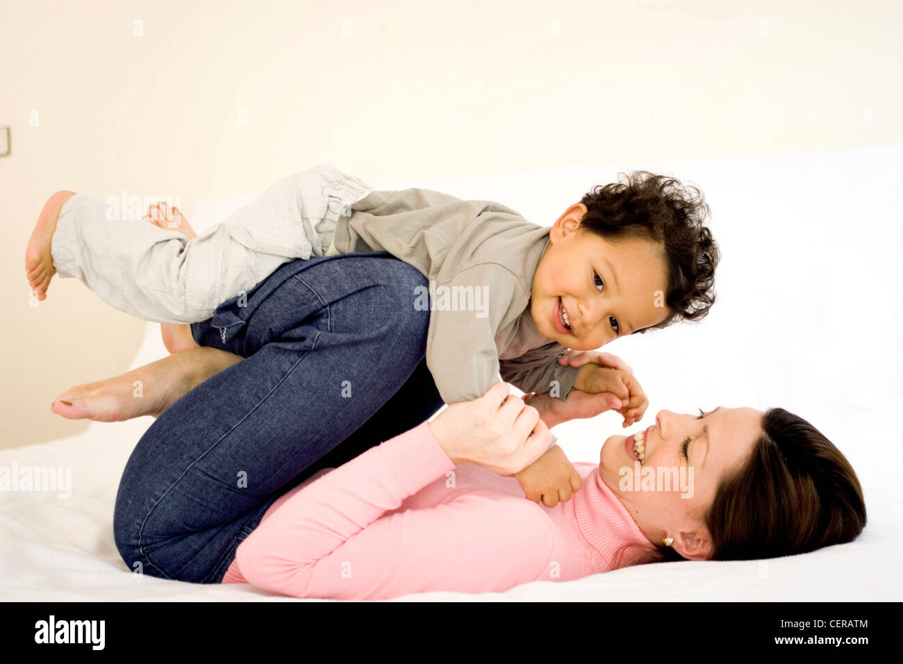 Weibliche brünette Haare tragen rosa Rollkragen und blaue Jeans auf Rücken blickte lächelnd zeigt Zähne halten männliches Kind Stockfoto