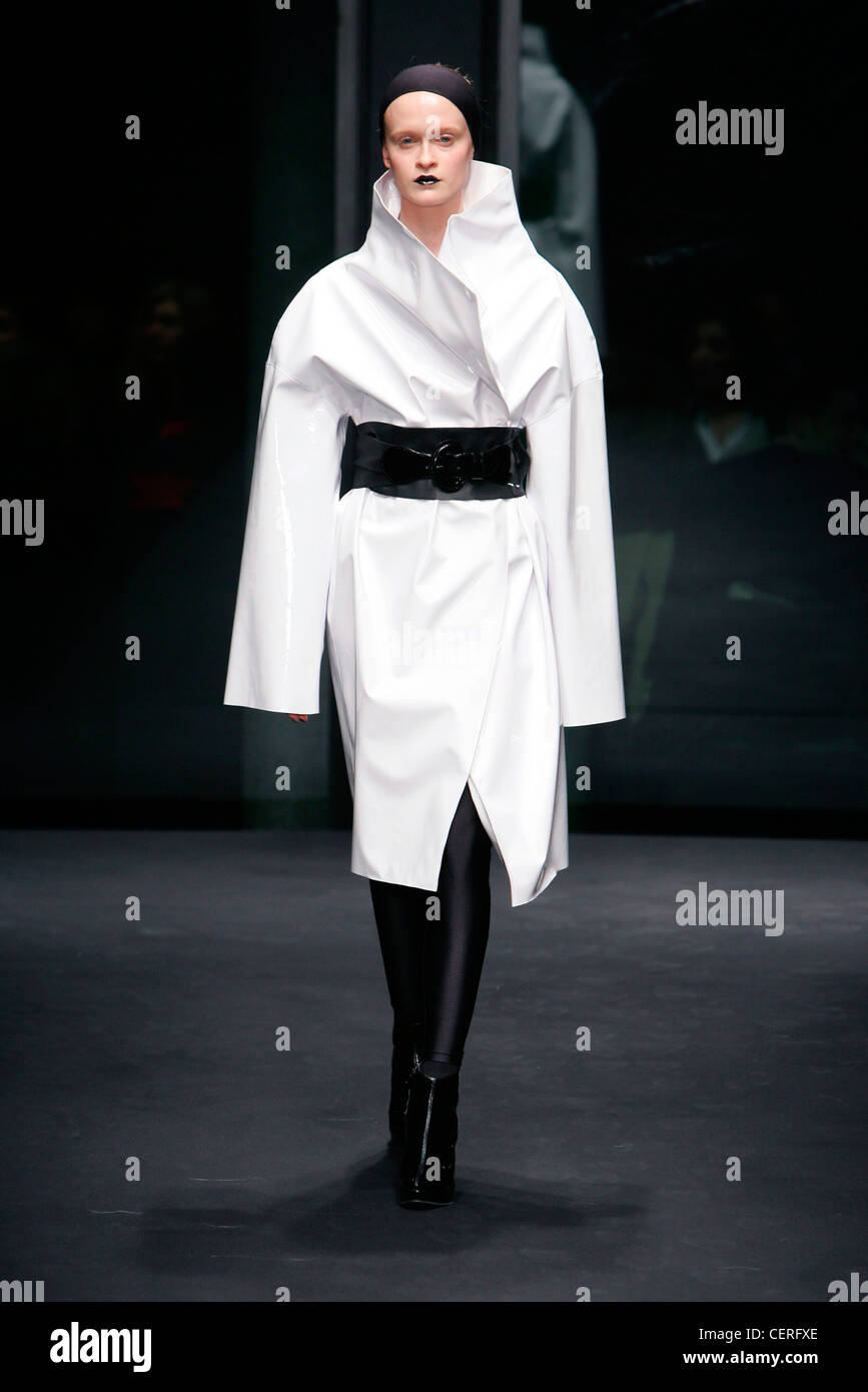 Schwarzen Stirnband, schwarze Lippen, weiße Kimono Stil Wrap Mantel mit großen Kragen und schwarzen breiten Gürtel, Lycra Leggings und Ankle-boots Stockfoto