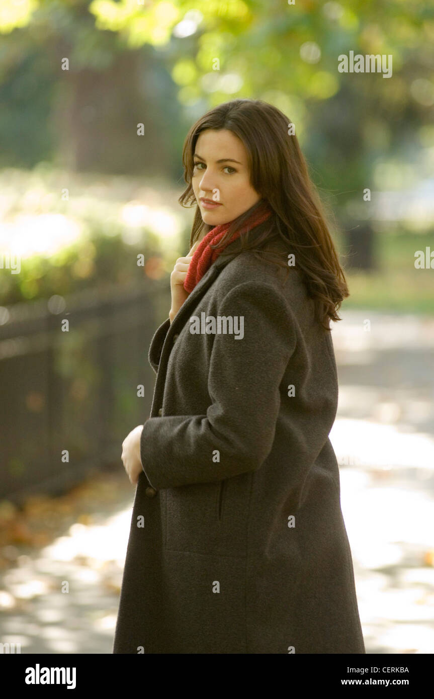 Weibchen tragen rote Rollkragen Pullover und braunen Mantel zu Fuß im park Stockfoto