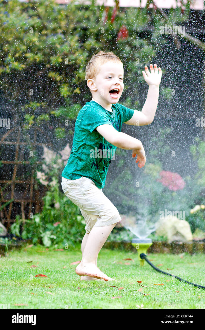 Glückliche kleine Junge spielt in das Spray aus einem Gartenschlauch Stockfoto