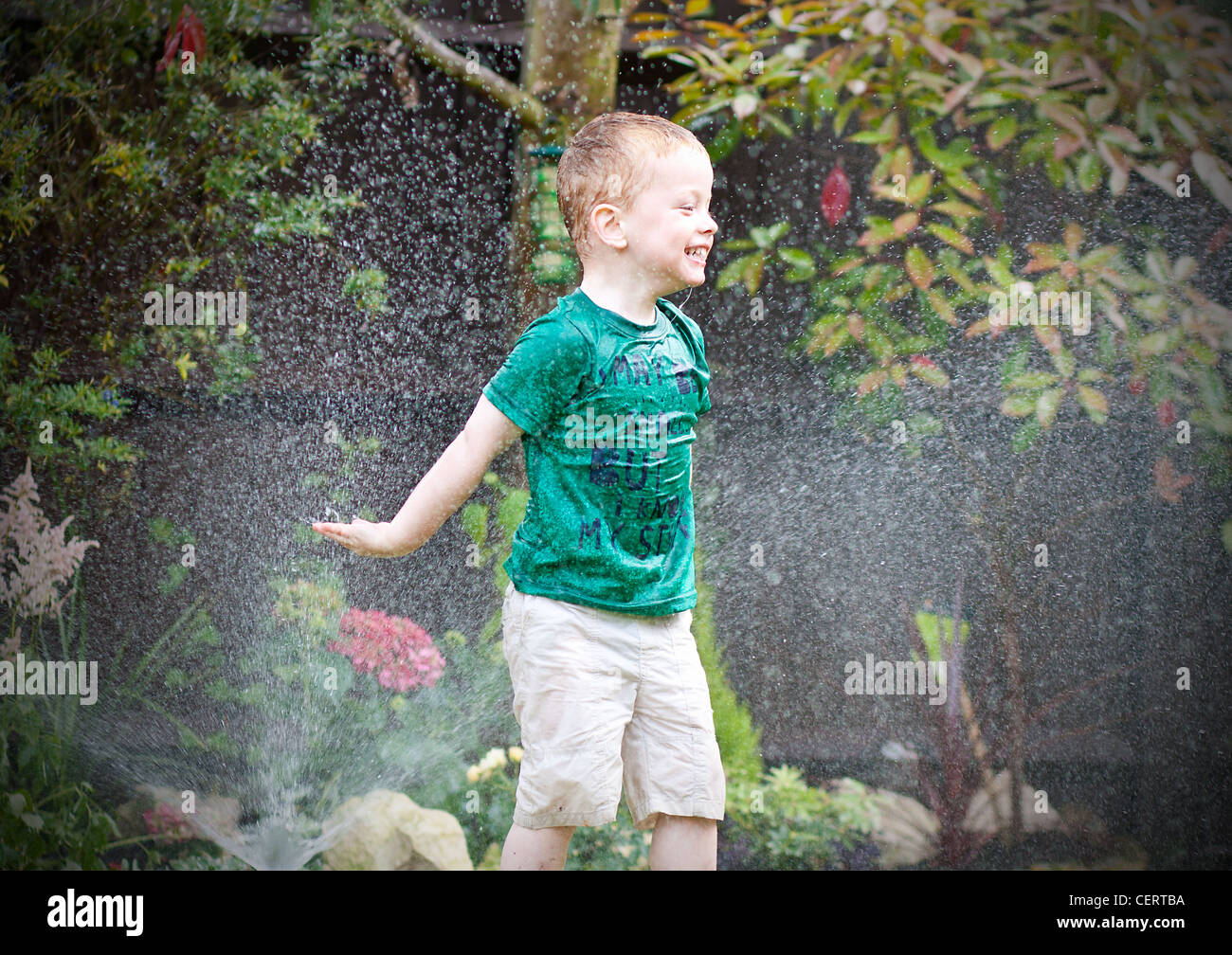 Glückliche kleine Junge spielt in das Spray aus einem Gartenschlauch Stockfoto