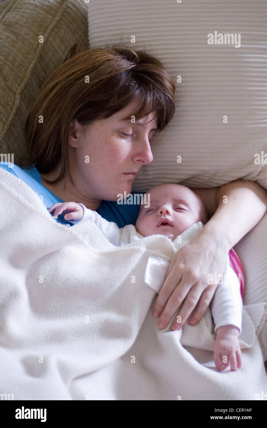 Weibliche drei Monate altes Baby liegen neben einer Erwachsenfrau, schlafend unter einer weißen Decke Stockfoto