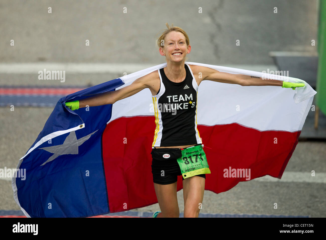 Glückliche Anglo Frau überquert die Ziellinie, feiert den Sieg durch die Anzeige von Texas Flagge beim Austin-Marathon in der Innenstadt von Austin, Texas Stockfoto