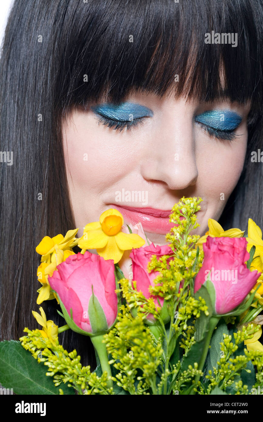 Weibchen mit Fransen brünette Haare tragen Fett Blau metallic-Lidschatten und rosa Lippenstift hält eine Reihe von Frühlingsblumen, Stockfoto