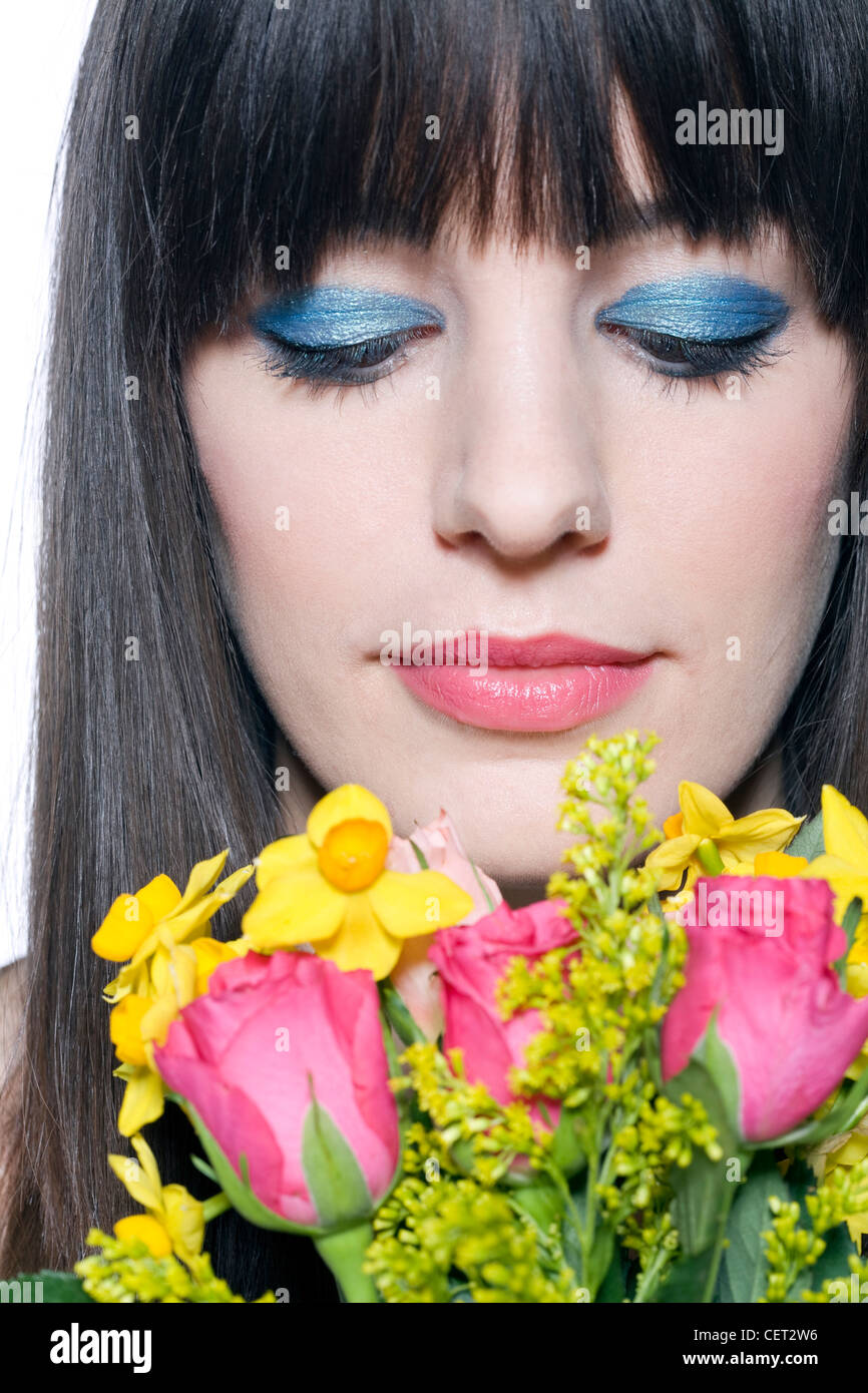Weibchen mit Fransen brünette Haare tragen Fett Blau metallic-Lidschatten und rosa Lippenstift hält eine Reihe von Frühlingsblumen, Stockfoto
