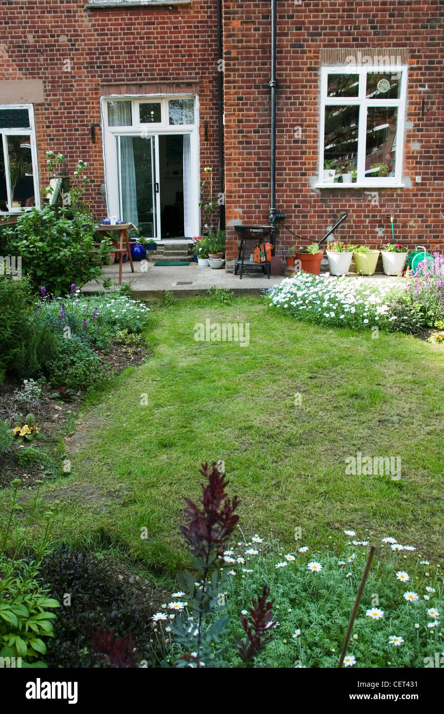 Renovierte Wohnung Exteriof Haus mit Schiebetüren, einen Rasen Garten mit Blumenrabatten und Topfpflanzen Stockfoto