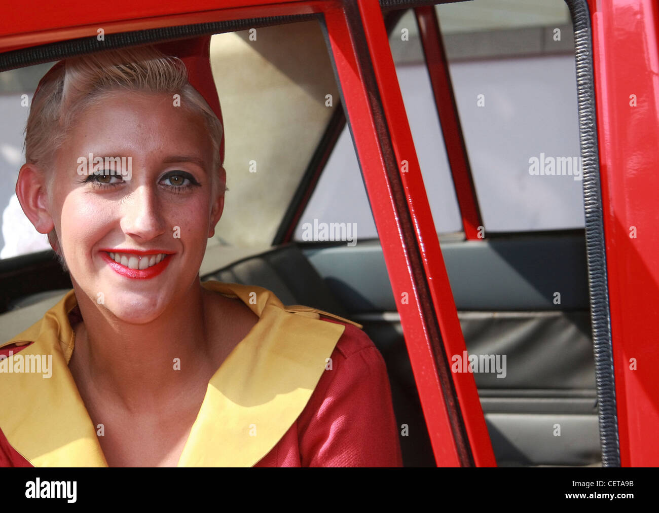 Blonde Glamour-Girl posiert in roten Auto beim Goodwood Revival. Stockfoto