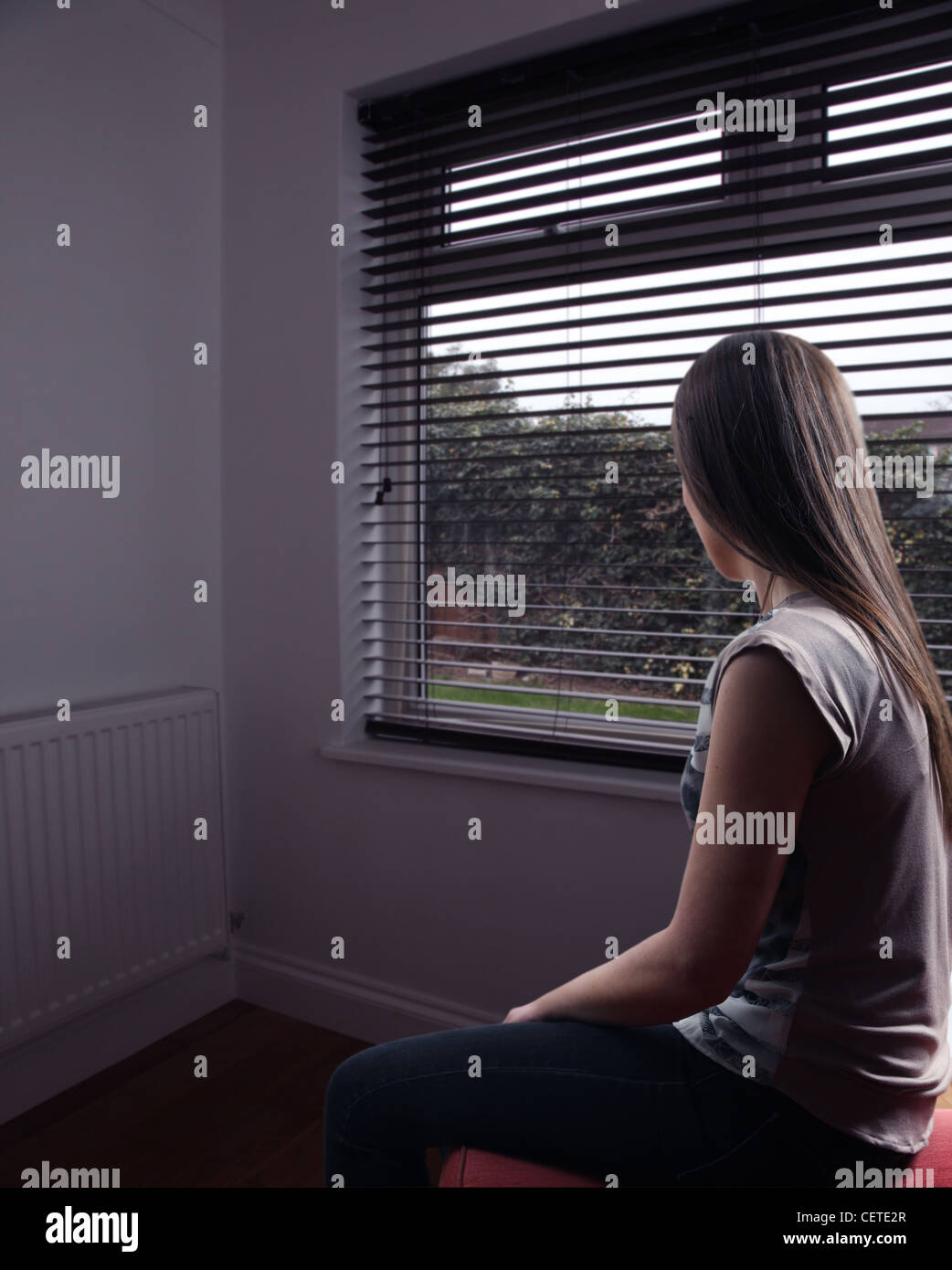 Rückansicht des eine nachdenkliche junge Frau sitzt allein der Blick aus einem Fenster. Stockfoto