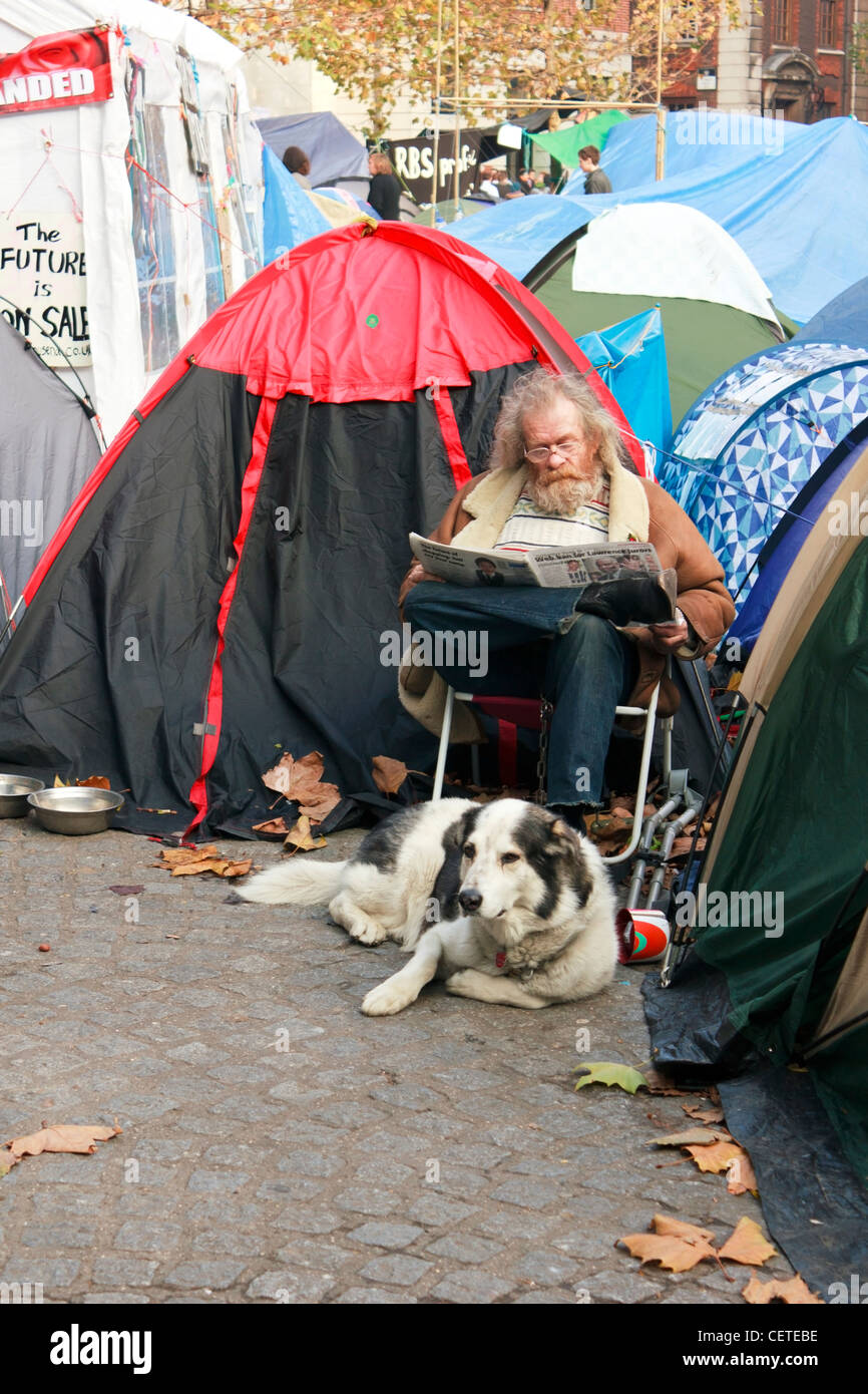 Ein Demonstrant besetzen London sitzt unter der Zelte mit seinem Hund lesen Zeitung vor der St. Paul Kathedrale, London Stockfoto