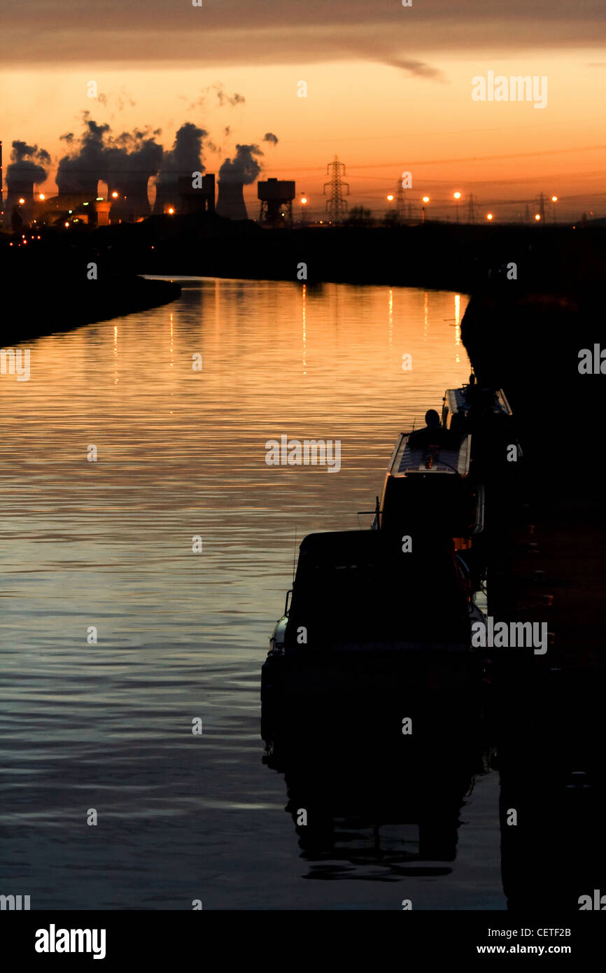 Ein Blick über Wasser, Rauch aufsteigt aus Industrieschornsteine bei Sonnenuntergang in Pontefract. Stockfoto