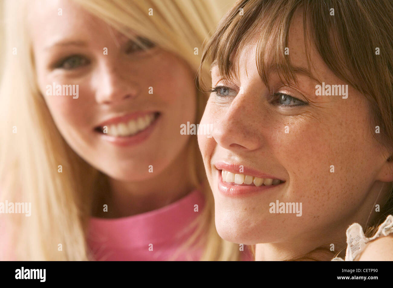 Weibchen auf recht lange brünette Haare, die wir auf Seite lächelnd, Weiblich auf linke lange blonde Haare, die auf Kamera Lächeln, Creme Stockfoto