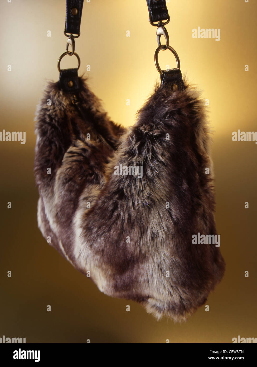 Braune Handtasche aus Kunstfell, aufgehängt mit Lederriemen vor einem warmen Studiohintergrund, die Textur und Wintermode hervorhebt. Stockfoto