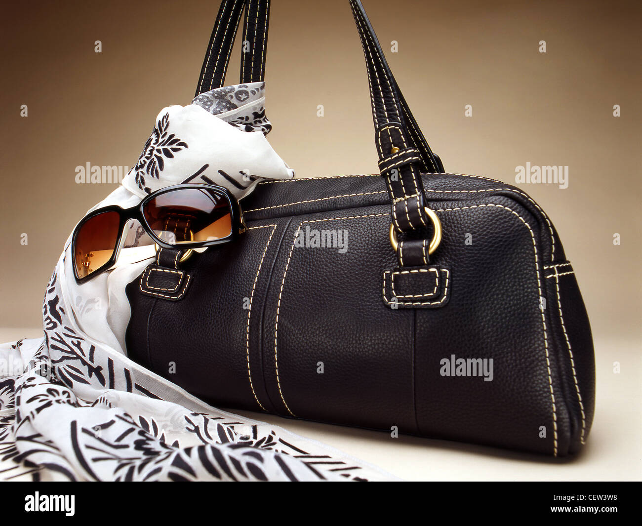 Handtasche aus schwarzem Leder mit gemustertem Schal und Sonnenbrille, fotografiert im Studio vor einem neutralen Hintergrund. Stockfoto