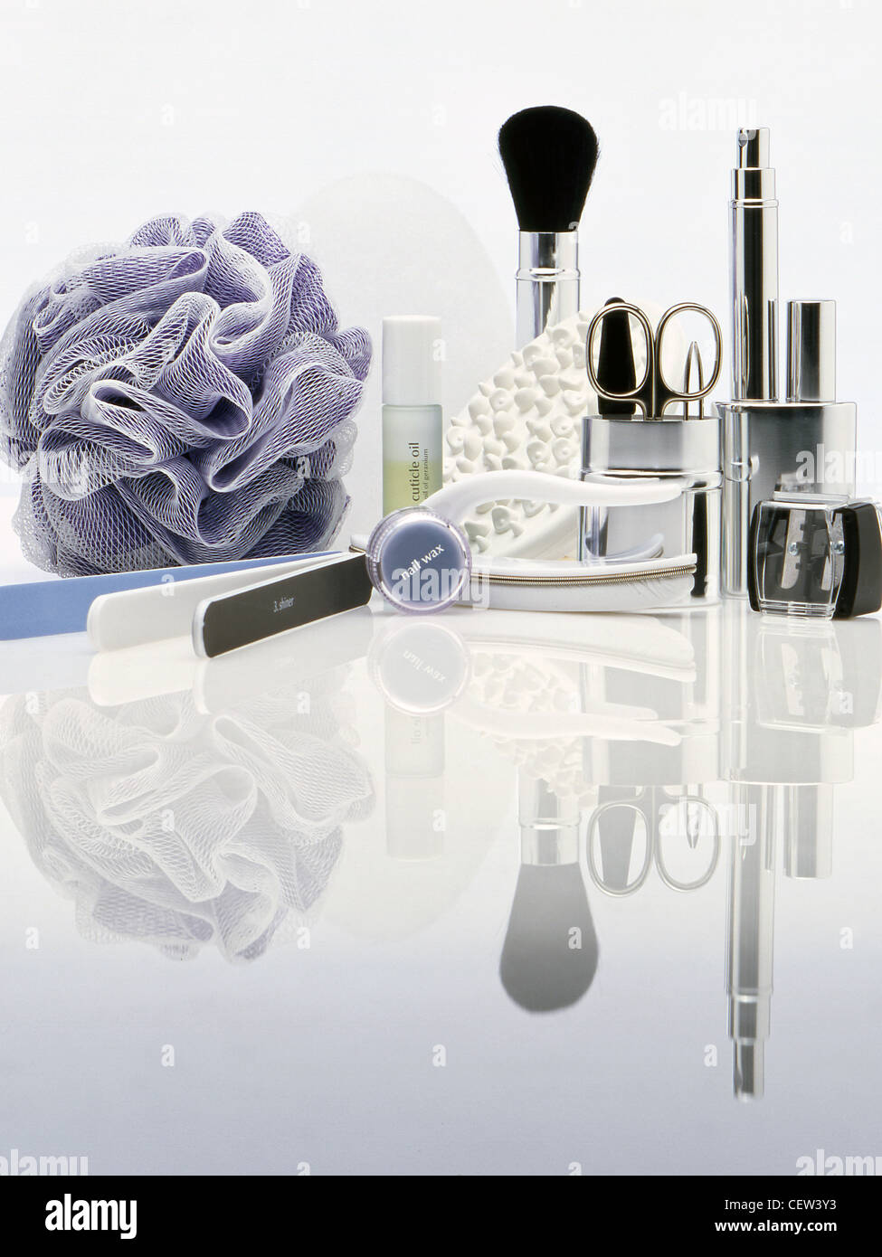 Verschiedene Kosmetik- und Pflegewerkzeuge, einschließlich Make-up-Bürste, Schere, Nagelpflegeartikel und Badeschwamm, auf einer weißen reflektierenden Oberfläche angeordnet. Stockfoto