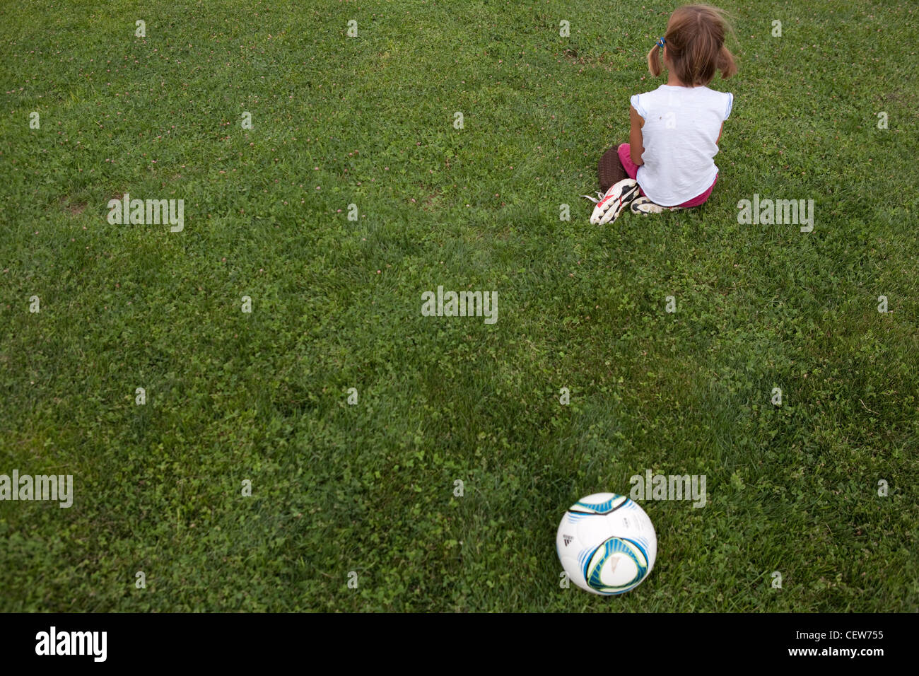 Kleines Mädchen mit dem Rücken wandten sich von einem Fußball auf einer Wiese. Stockfoto