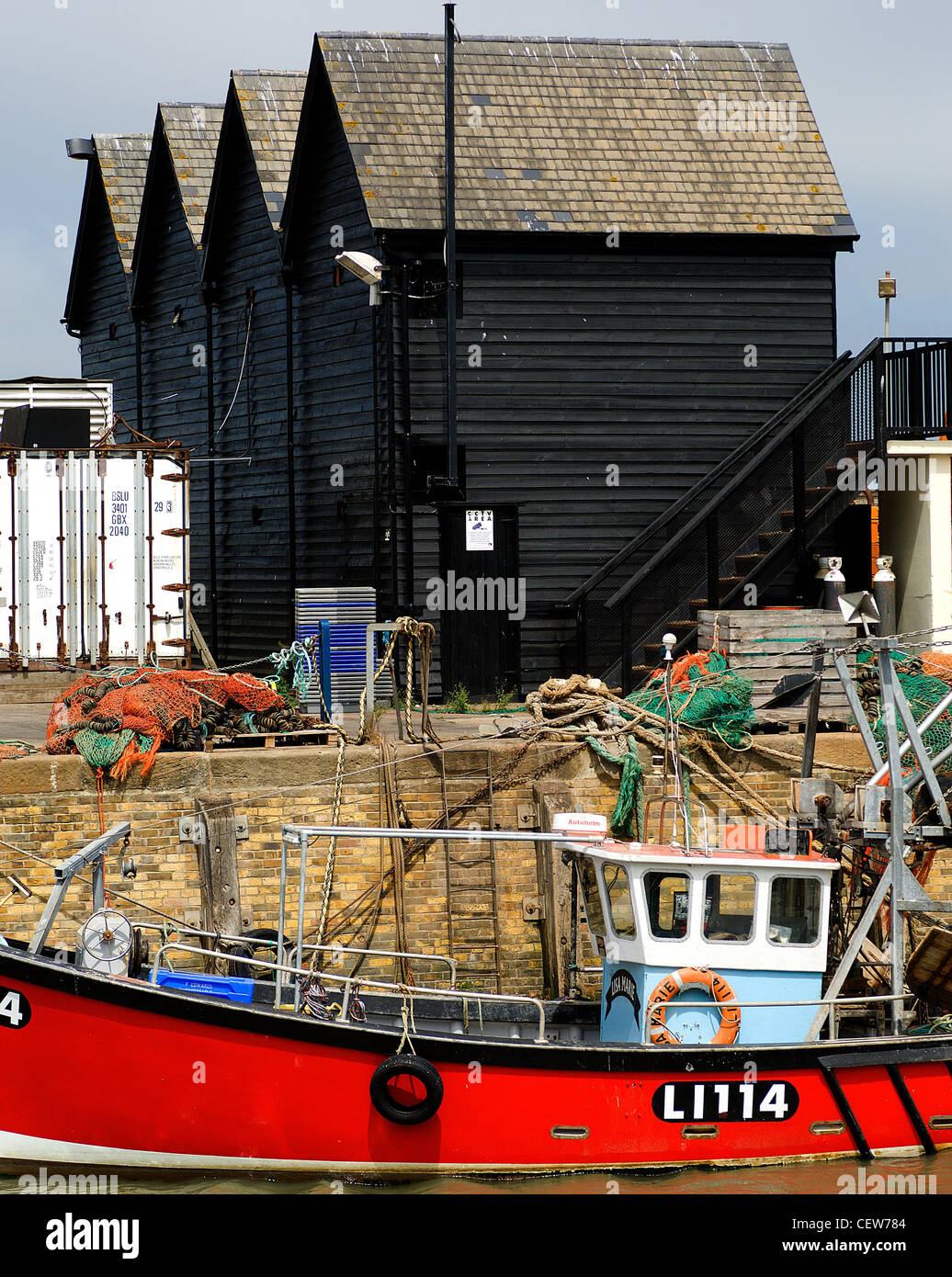 Eine moderne Fischerboot vor Anker in Whitstable, Kent, vor einigen der traditionellen Auster Schuppen für die die Stadt berühmt ist. Stockfoto