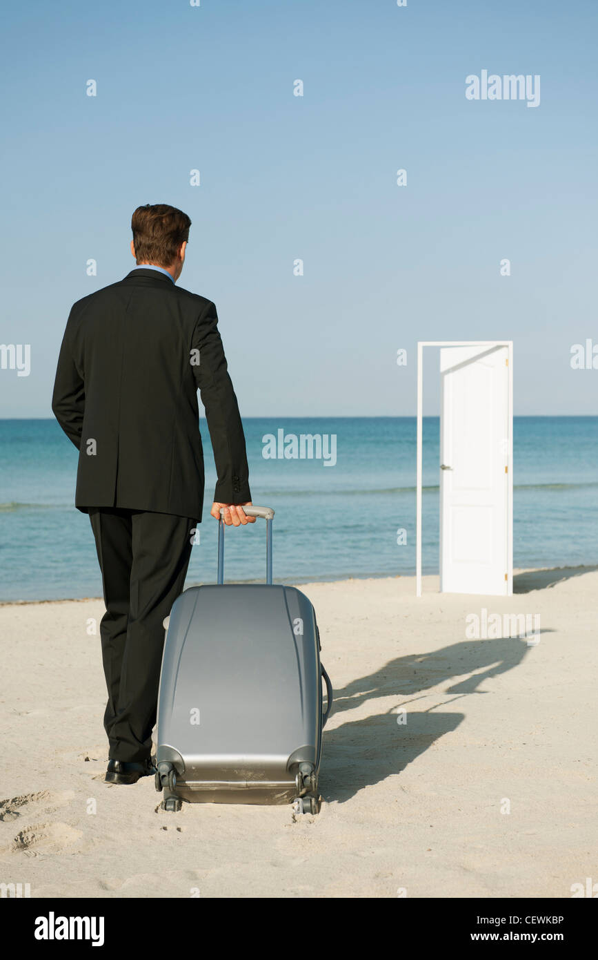 Geschäftsmann ziehen Koffer am Strand, halb offene Tür im Hintergrund Stockfoto