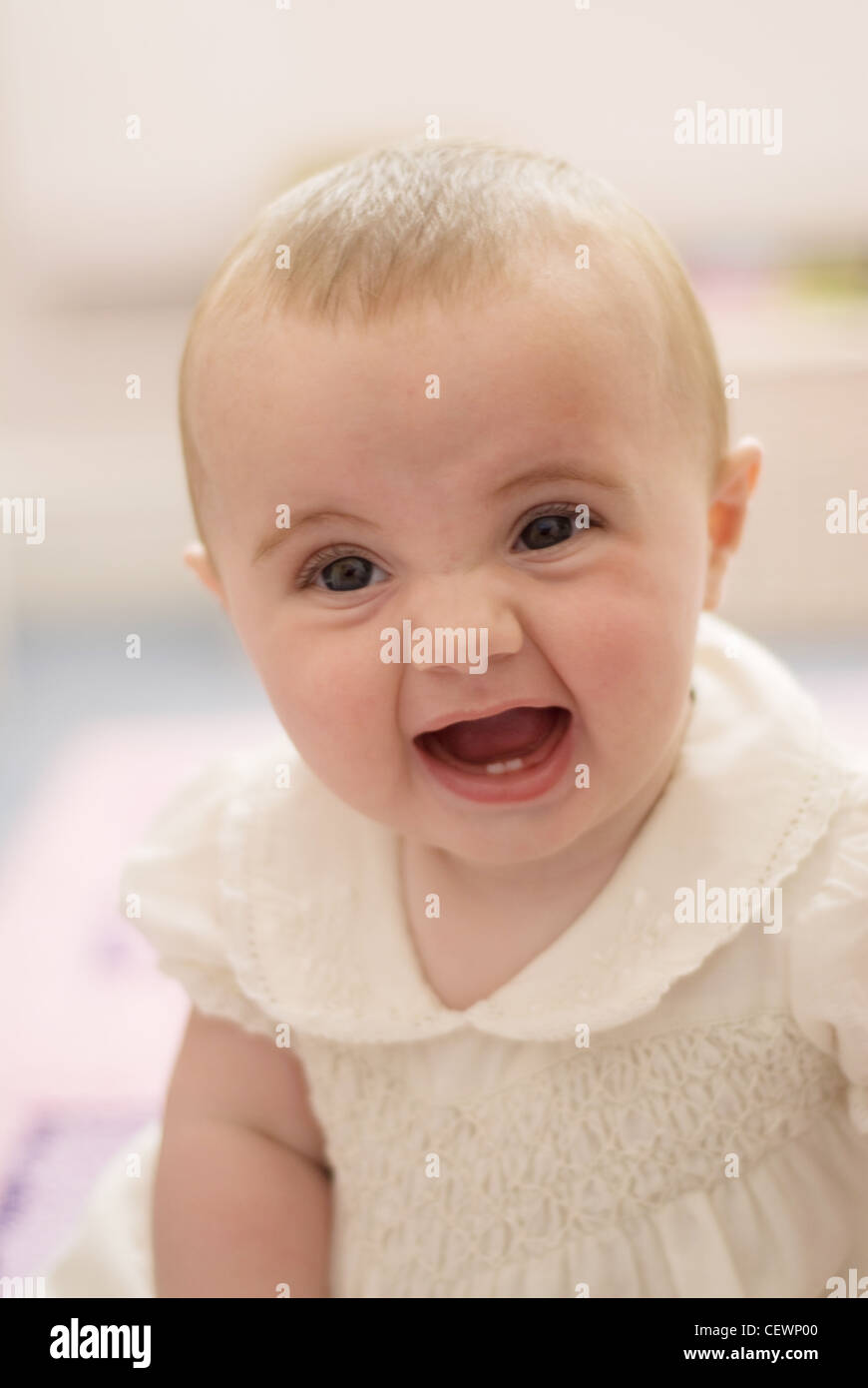 Ein weibliches Baby, trägt ein weißes Kleid, sitzen auf dem Boden, Mund öffnen zeigt zwei unteren Zähne, Joel Penn nachschlagen Stockfoto