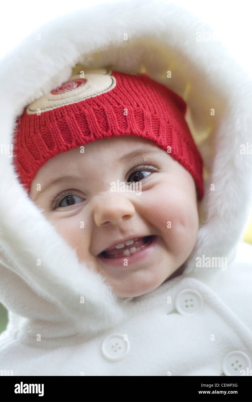 Ein weibliches Baby gestrickt mit einem roten Hut und weißen Kapuzen-Mantel mit Pelzbesatz, Lächeln, wir auf der Seite Joel Penn Stockfoto