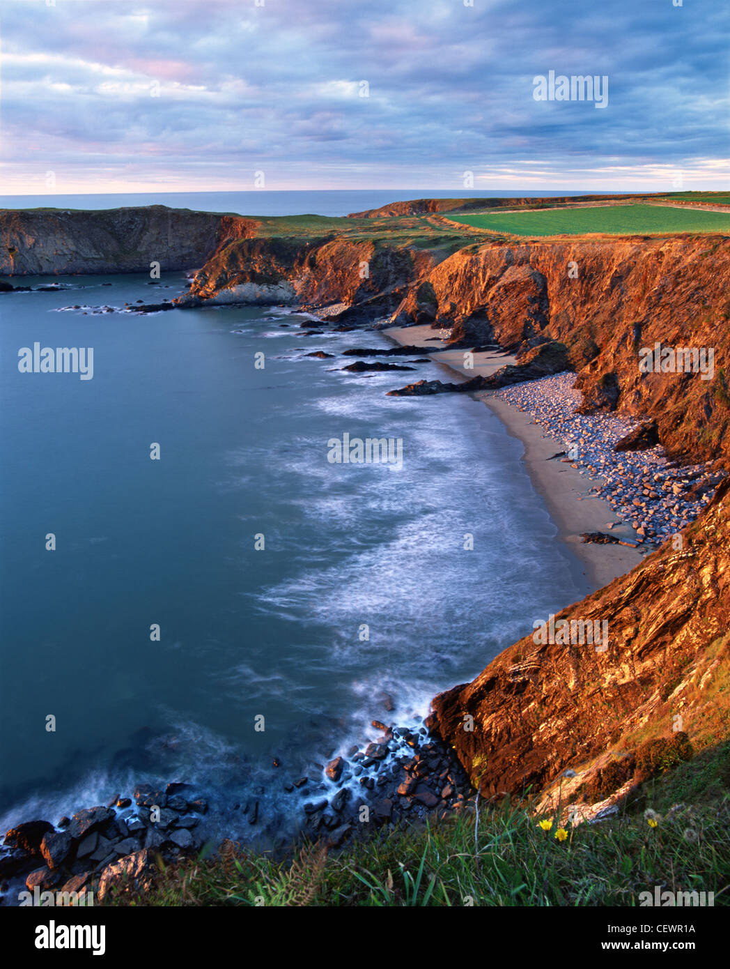 Die weichen Felsen und Felsbrocken übersäten Strand von Traeth Llyfn Bucht sind ein reichhaltiges warmes Gold von der untergehenden Sonne gemalt. Stockfoto