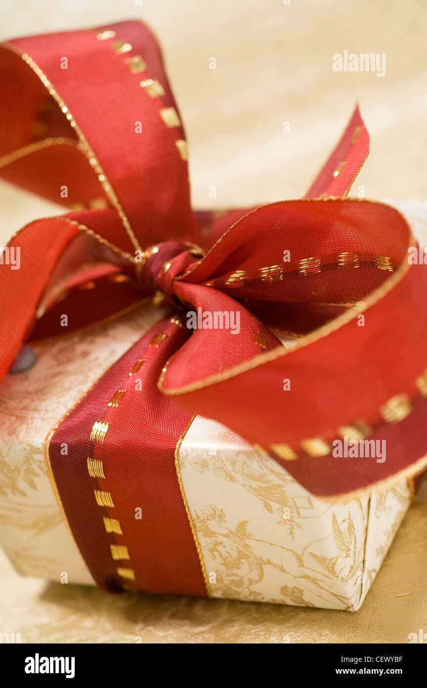 Weihnachtsgeschenk mit breiten roten und goldenen Schleife gebunden in großen Bogen an der Spitze mit Creme und gold Toile de Jouy-Stil-Papier eingewickelt Stockfoto