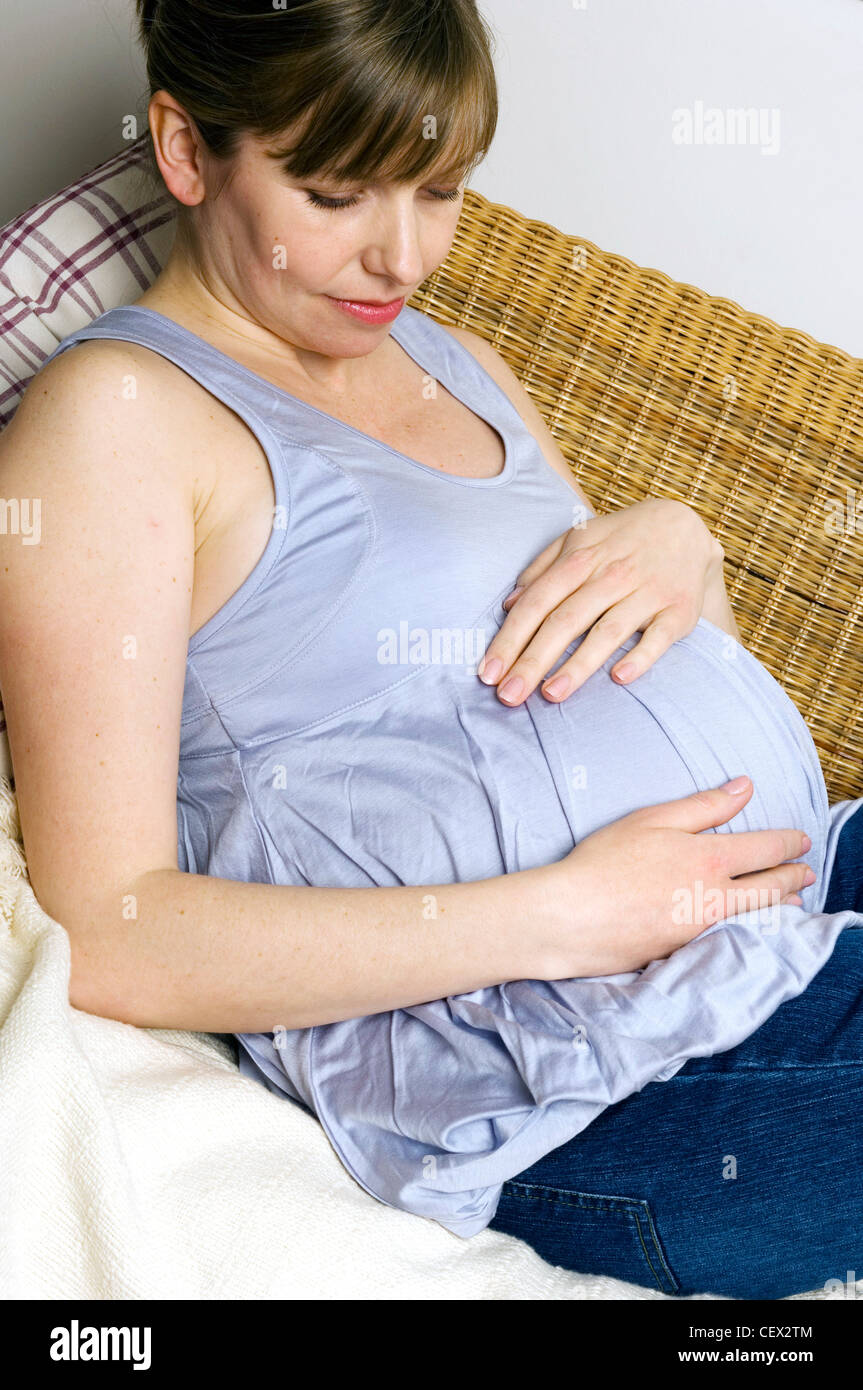 Trächtige Weibchen auf Wicker Sofa liegend mit Hände ruhen auf Stoß Stockfoto