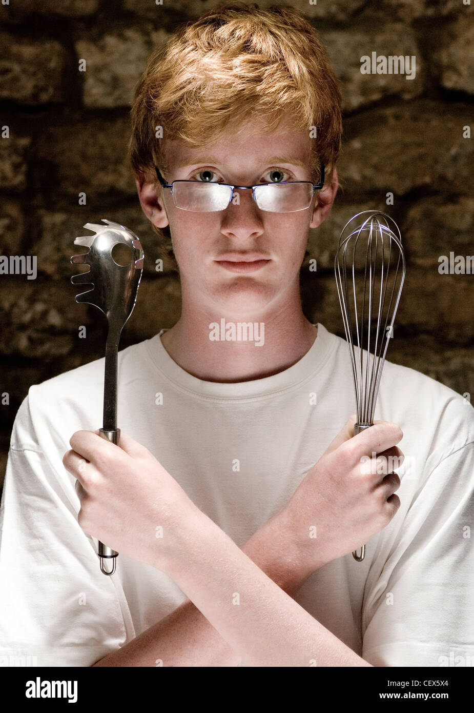 Männliche Teenager auf der Suche direkt in die Kamera hielt ein Spaghetti-Löffel und einem Schneebesen Stockfoto
