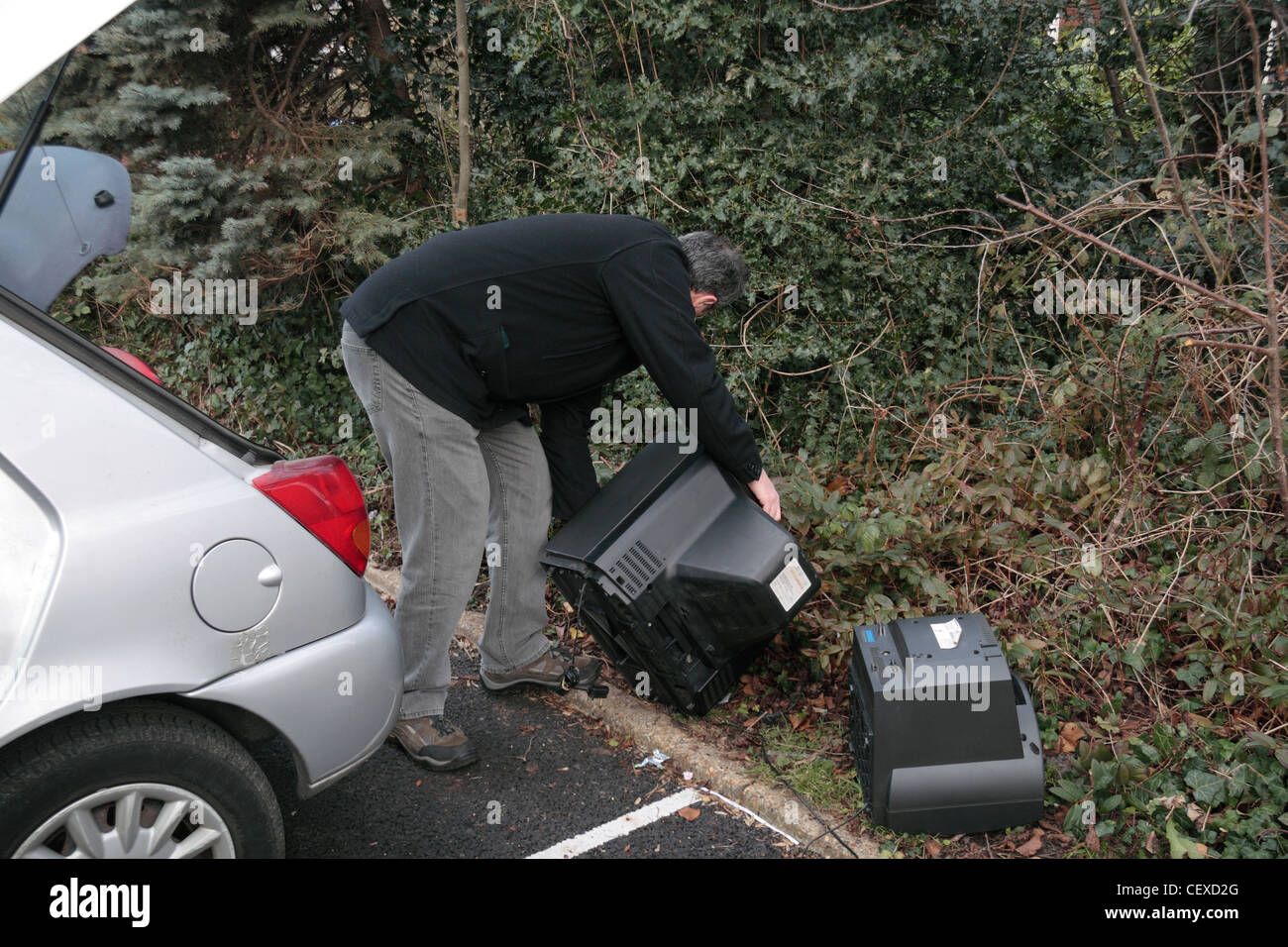 Ein Mann illegal dumping (Fly tipping) einige große Gegenstände, einschließlich Fernsehern auf der Seite ein Parkplatz zur Verfügung. (Gestellt). Stockfoto