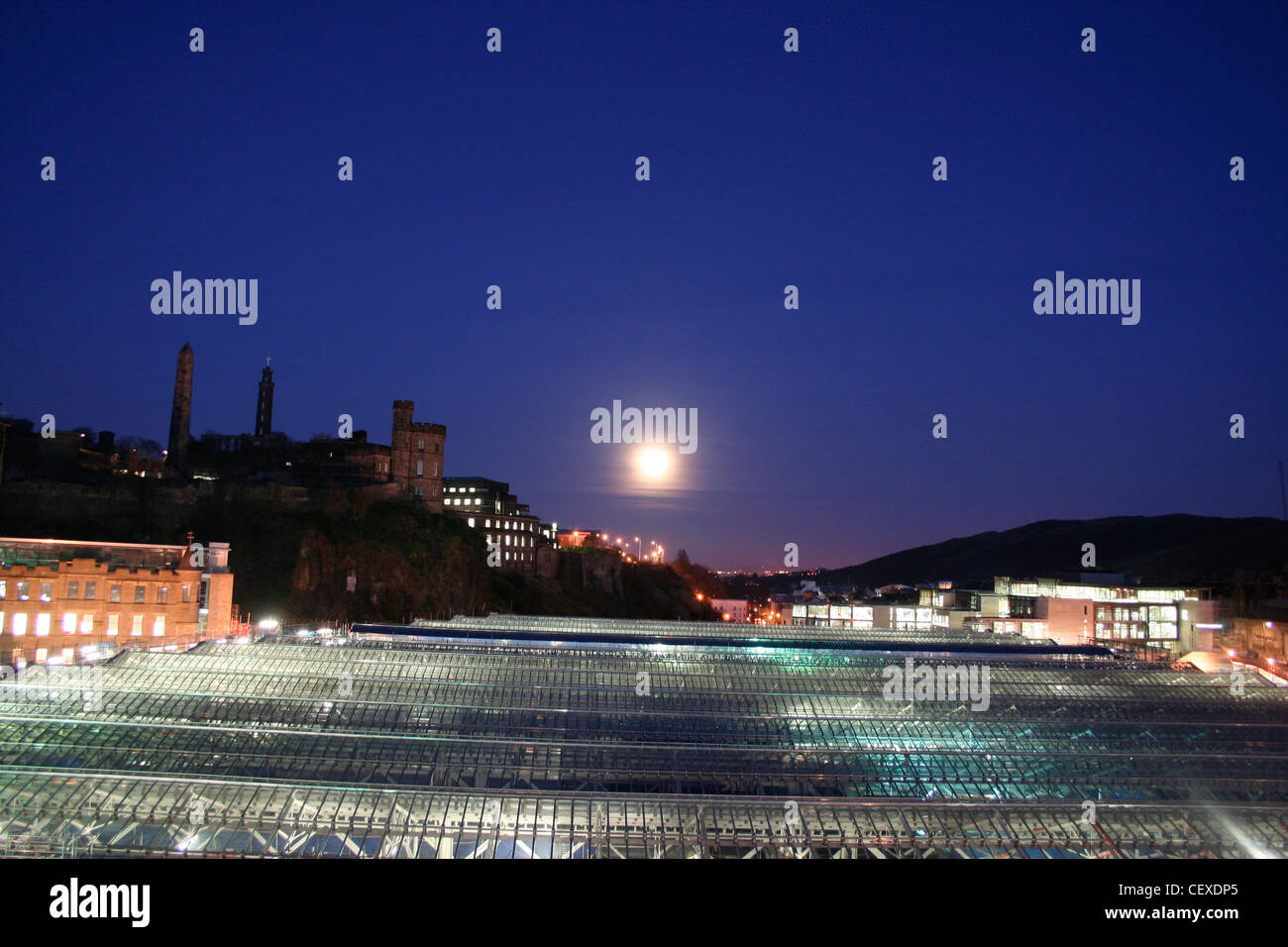 Blick über Edinburgh Waverley Station von North Bridge Skyline Calton Hill mit großen Mond im dunklen blauen Nachthimmel. Stockfoto