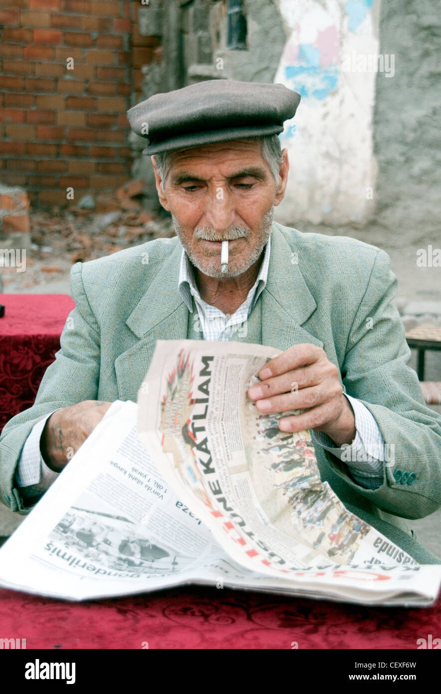 Ein alter kurdischer Mann, der in einem Café im Freien in der Stadt Diyarbakir im östlichen Anatolien der Türkei eine Zigarette raucht und eine Zeitung liest. Stockfoto