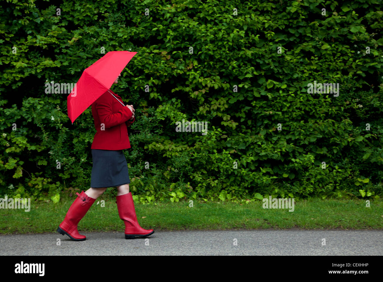 Foto einer Frau in rot zu Fuß entlang einer Straße mit ihrem Schirm bis Stockfoto