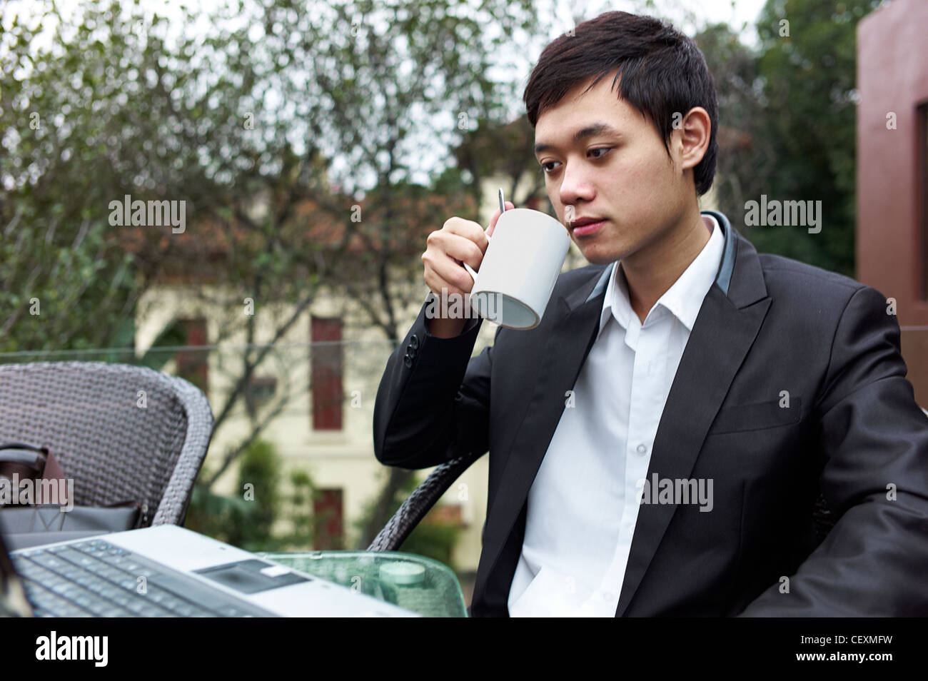 Ein junger Geschäftsmann trinkt Kaffee während der Arbeit an seinem Laptop in einem Straßencafé in Hanoi, Vietnam Stockfoto