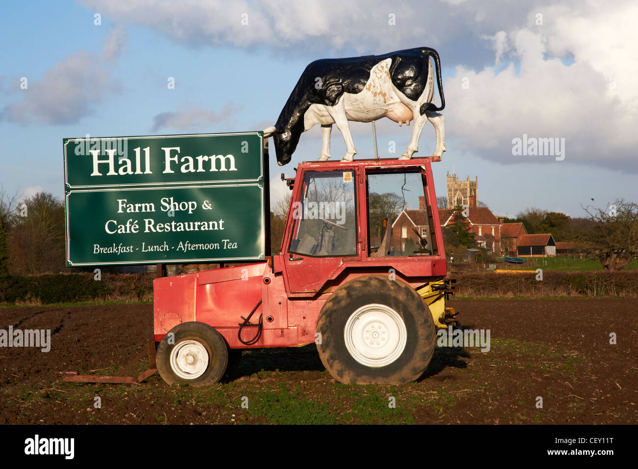 Ein Leben Größe Modell einer friesischen Kuh auf dem Dach von einem kleinen roten Traktor in schlammigen Feld mit Werbung Schild für einen Hofladen. Stockfoto