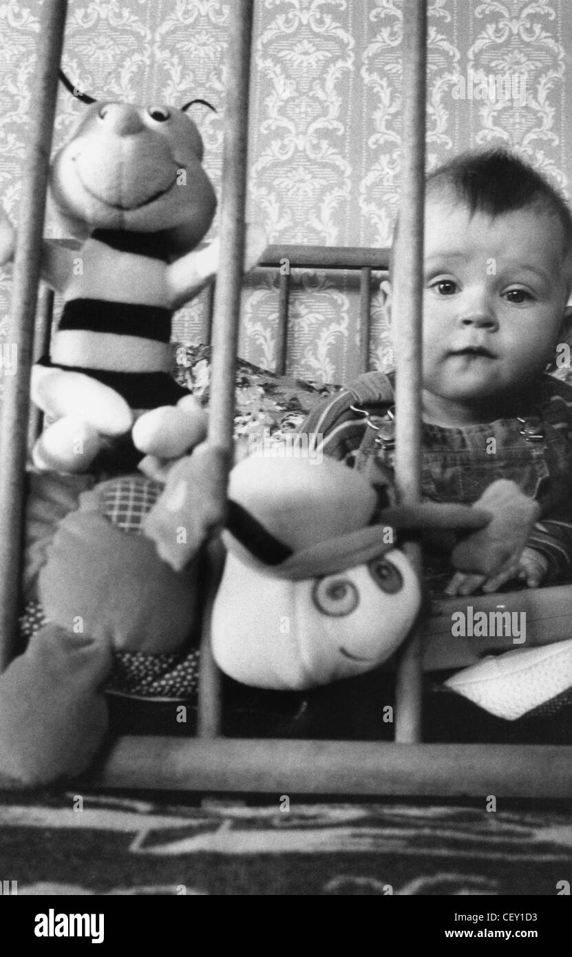 ALFI zu Hause "Kleinkind im Kinderbett spielt mit Spielzeug, sitzen wir auf Kamera mit schläfrigen Ausdruck Stockfoto
