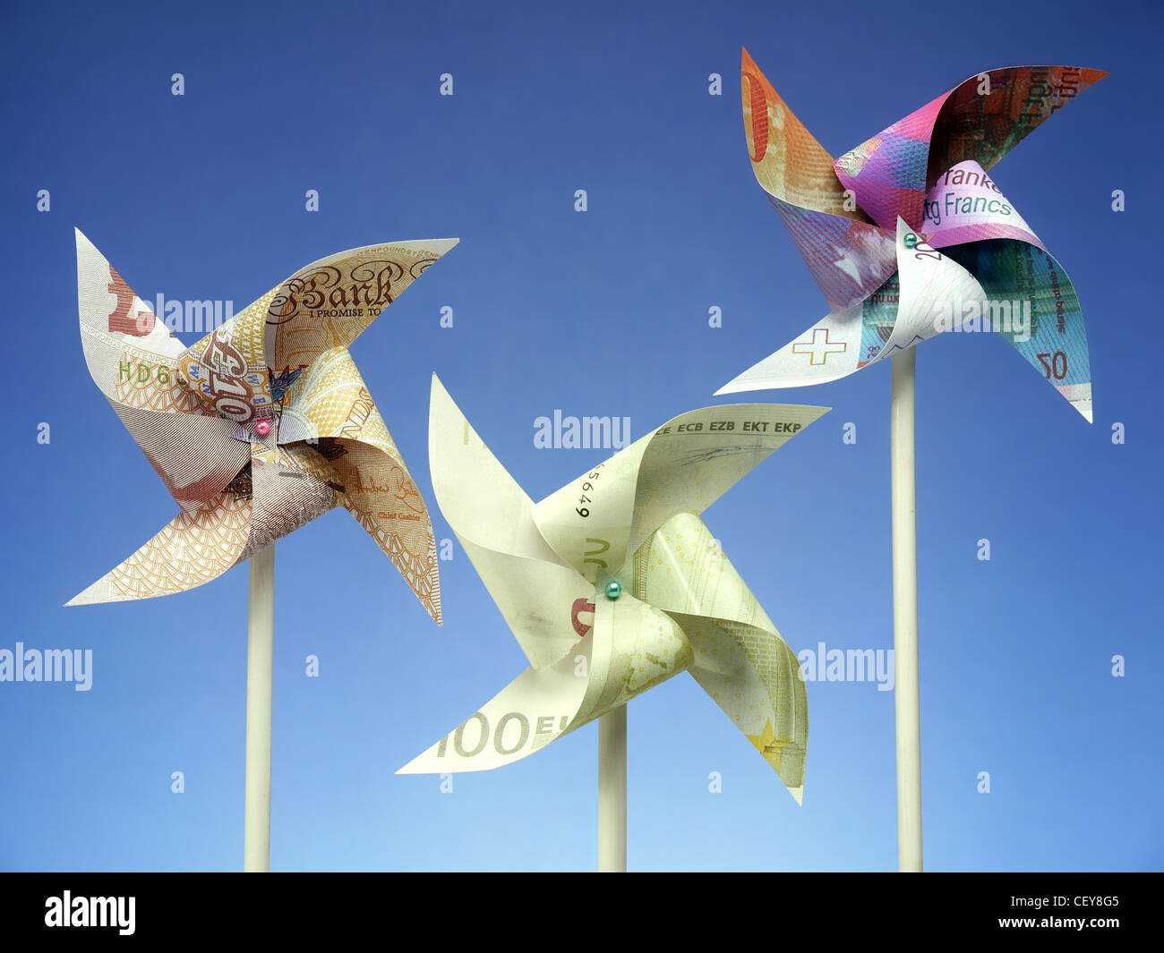 Drei große europäische Banknoten - Euro, Schweizerfranken und britische Pfund schneiden in Spielzeug Windmühlen gedreht auf blauem Hintergrund Stockfoto