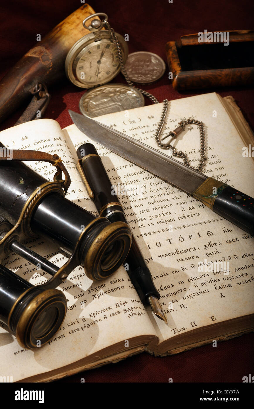 Alte Dinge platziert auf einem offenen alten kyrillischen Buch - ein Montblanc Stift, eine Uhr, ein Fernglas, ein Messer und andere. Stockfoto