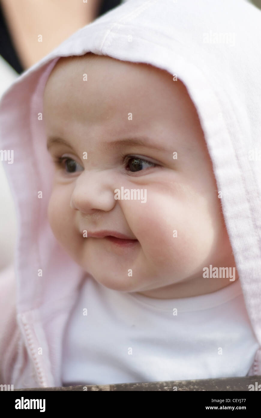 Ein weibliches Baby, tragen eine weiße Spitze und rosa Kapuzenjacke, ernsten Blick beiseite Joel Penn Stockfoto