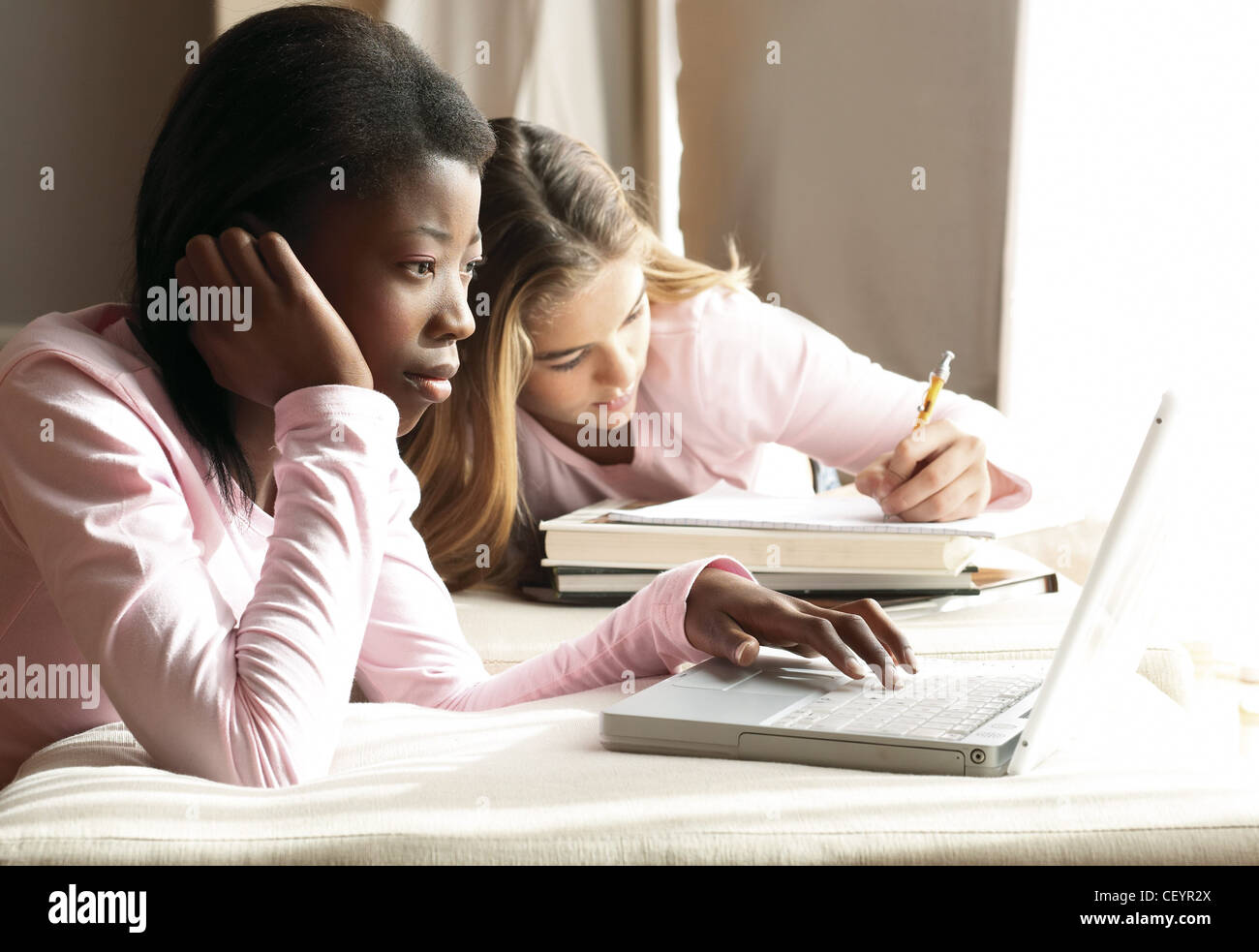 Zwei Mädchen beide trägt eine rosa lange Ärmel Top Mädchen langes blondes Haar schreiben auf Notizpapier stützte sich auf Bücher, Mädchen schwarze Haare Stockfoto