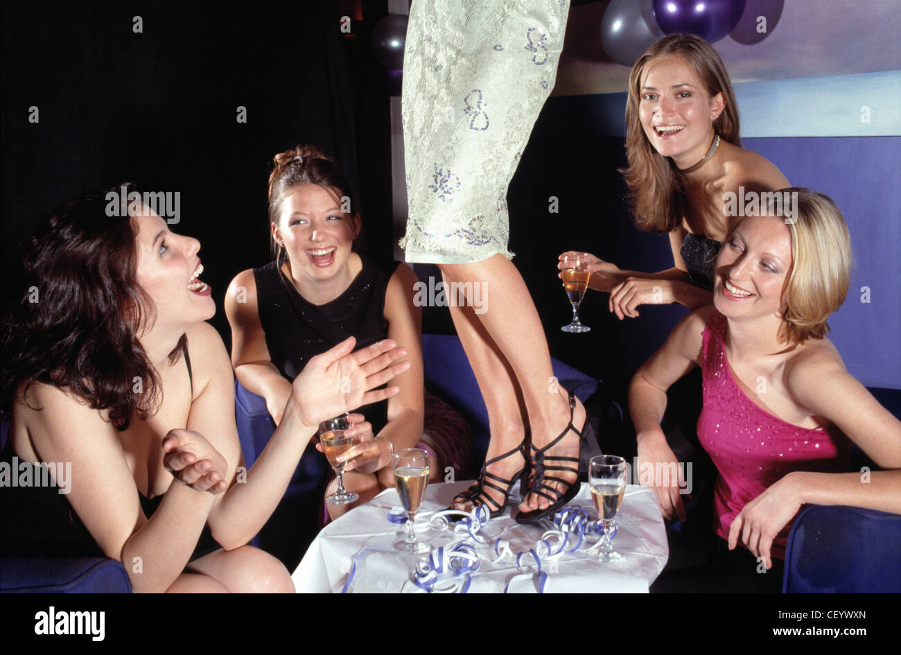 Fünf Frauen gekleidet in Abendkleidern, saß an einem Tisch trinken Champagner während einer weiblichen Tänze auf dem Tisch Stockfoto