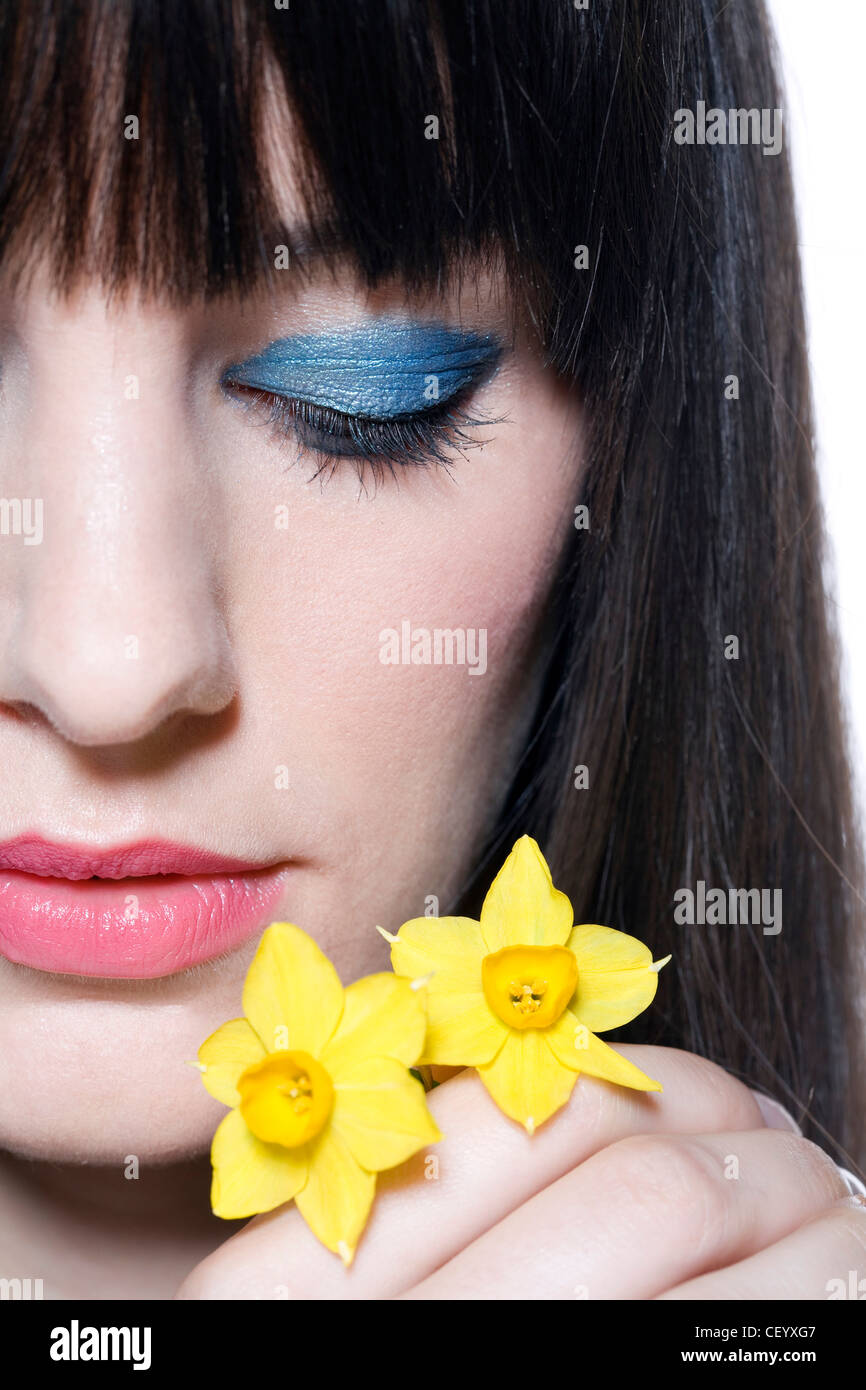 Weibliche Fransen brünette Haare, Fett Blau metallic-Lidschatten und rosa Lippenstift tragen, halten zwei Narzisse Blumen, ernsten, Stockfoto