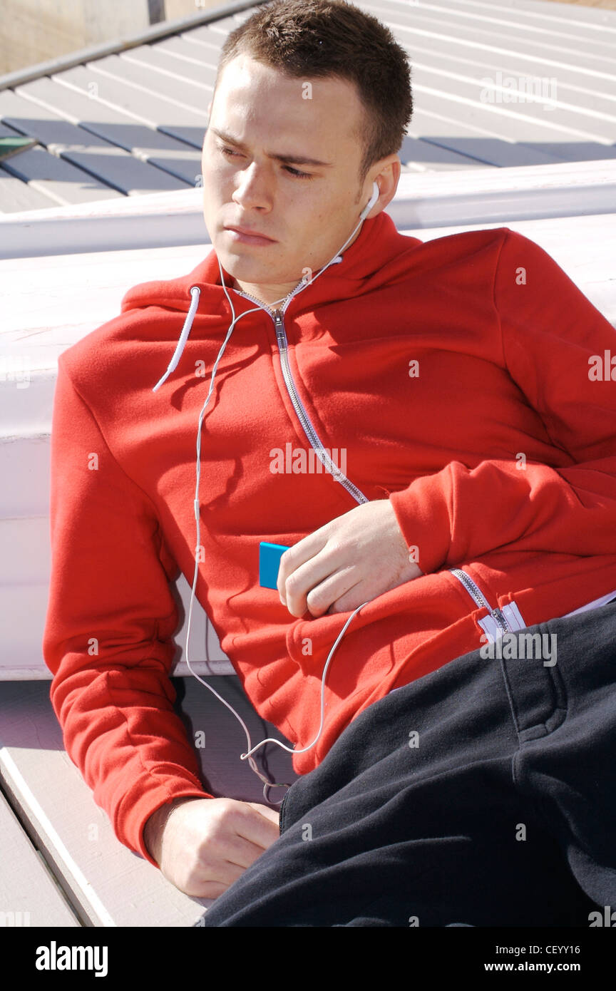 Männlichen kurze brünette Haare, trägt ein rotes Kapuzen-Sweatshirt und schwarzen Trainingsanzug Böden, hält eine i Pod mp Spieler in einer Hand Stockfoto