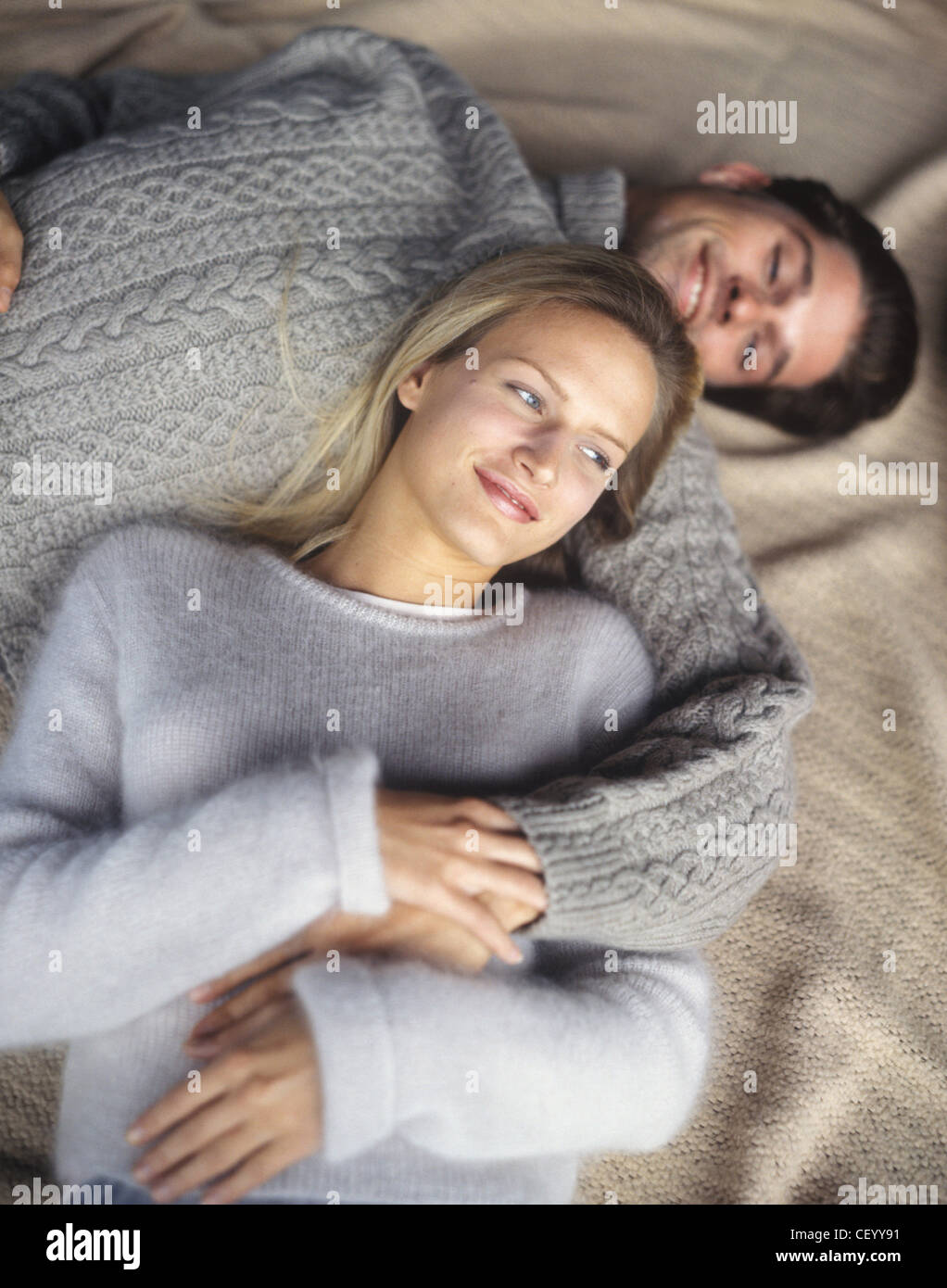 Lächelnde Frau mit blonden Haaren und Brünette Mail tragen graue Pullover, Kuscheln im Bett, Stockfoto