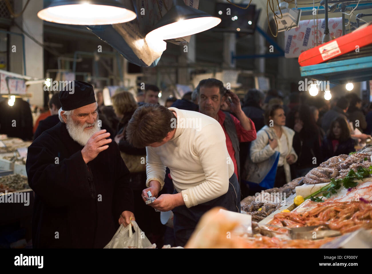 Griechisch-orthodoxe Priester segnet einen Fischhändler, wie er Fisch und Meeresfrüchte in Athen Zentralmarkt auf Athinas Street, Athen, Griechenland kauft Stockfoto